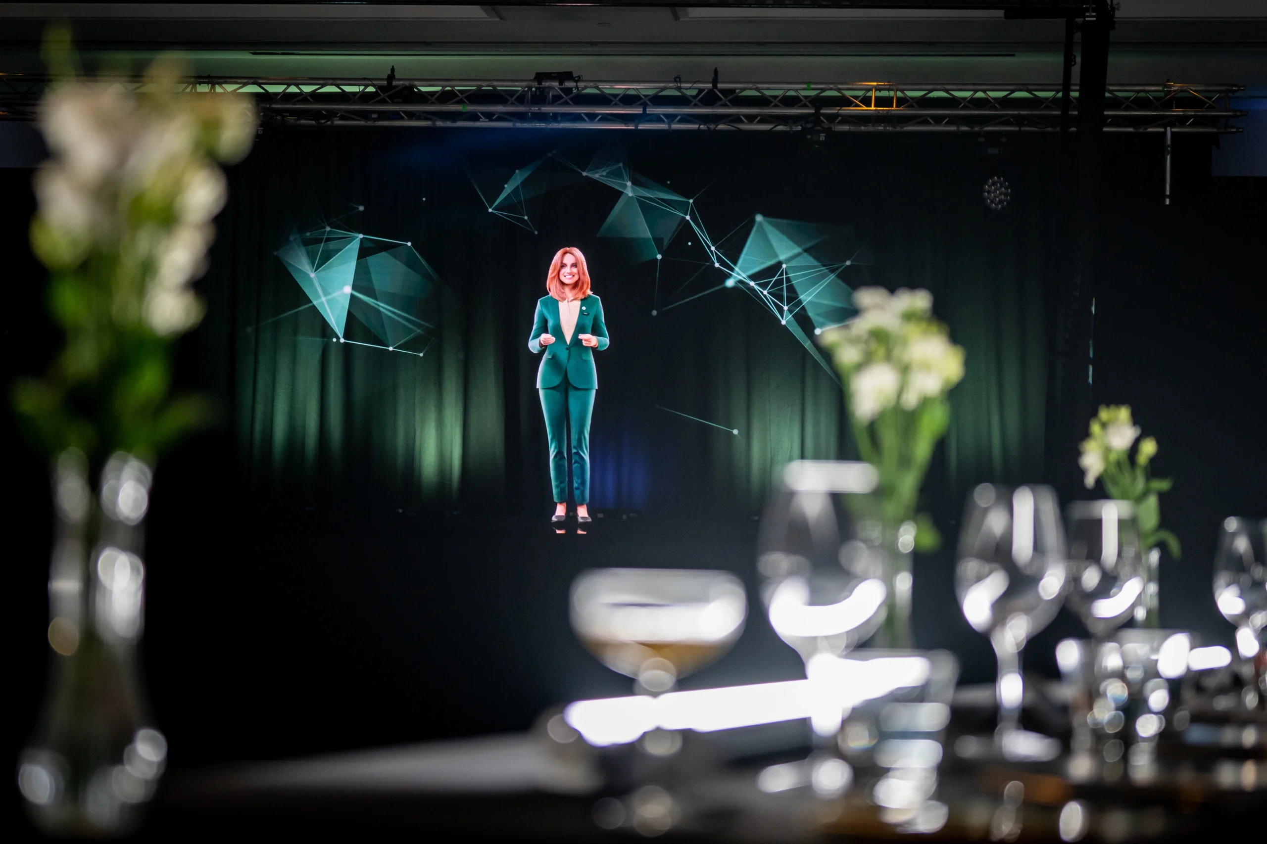 AI hologram Anna, a digital human in a green suit, on stage with network graphics at Pullman London