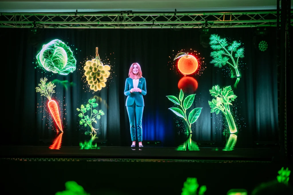 AI hologram Anna on stage surrounded by glowing illustrations of fruit and vegetables at Pullman London